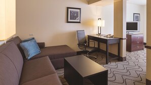 A hotel room with a sofa, a desk, a chair, a lamp, a television, and a dresser. - Spark by Hilton Central Point Medford (Central Point)
