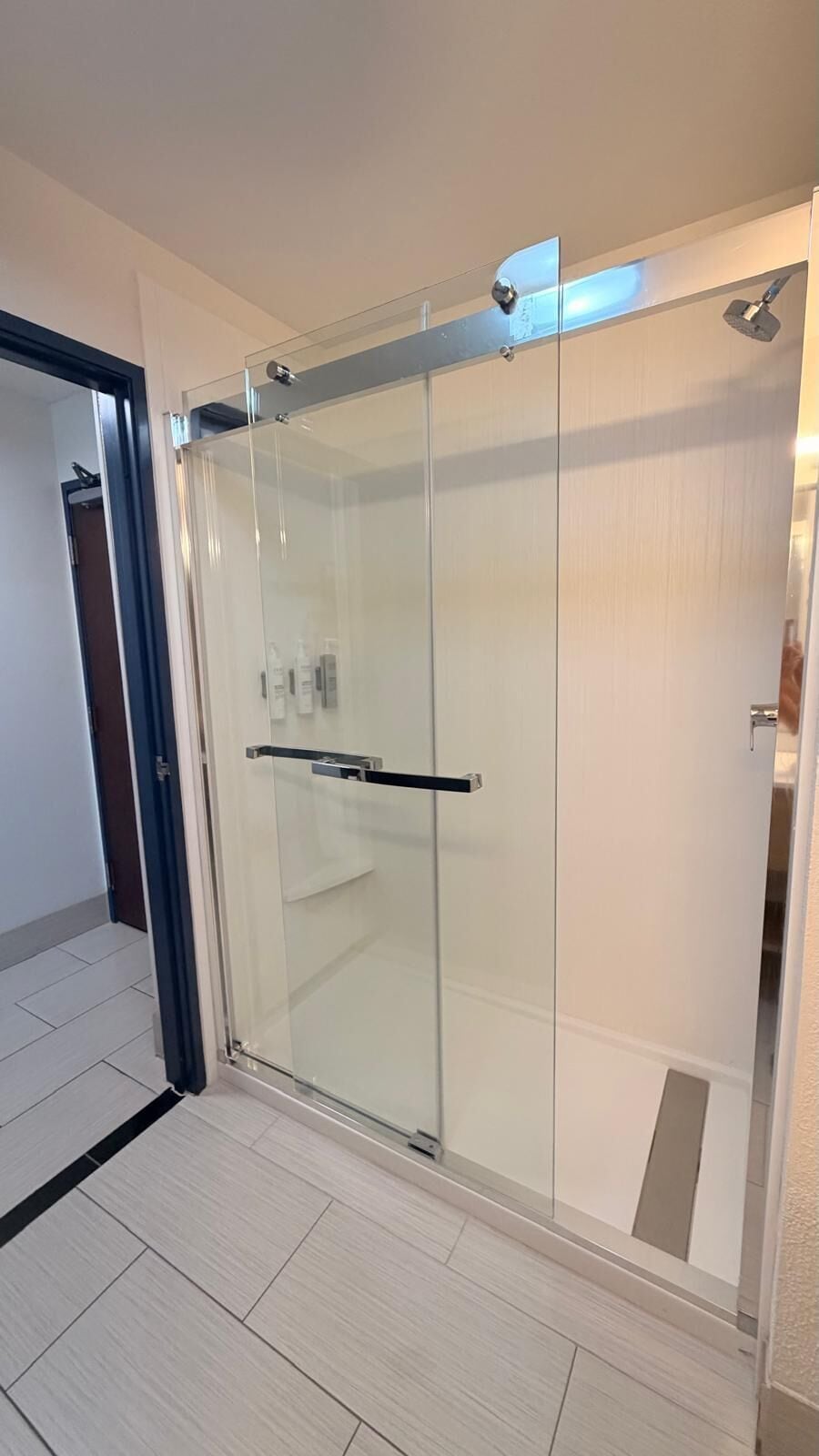 Un baño moderno con cabina de ducha de vidrio, suelo de baldosas blancas y ducha a la vista.