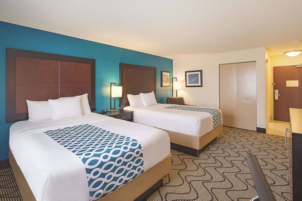 A hotel room with two beds, a desk, a chair, a nightstand, and a door.