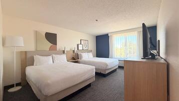A hotel room with two beds, a desk, a lamp, and a television.