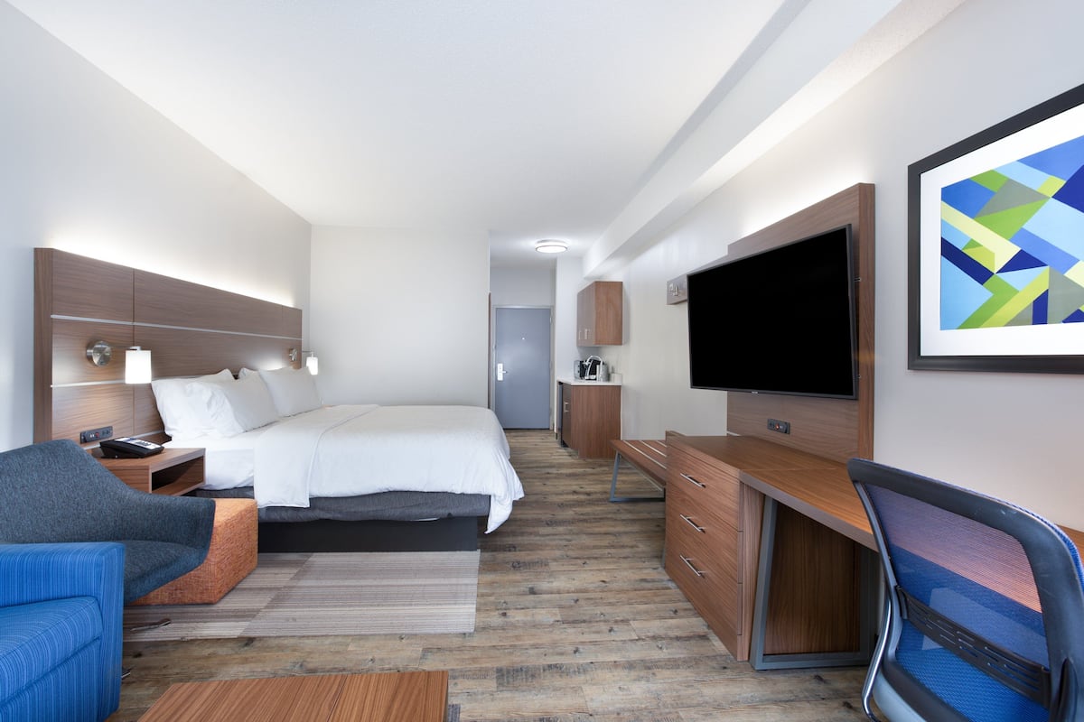 A modern hotel room with a bed, a desk, a TV, and a seating area.