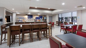 A spacious dining area with multiple tables and chairs, a counter with a menu, and a view of the outdoors through large windows. - Holiday Inn Express Hotel & Suites Morehead Cty by IHG (Morehead City)
