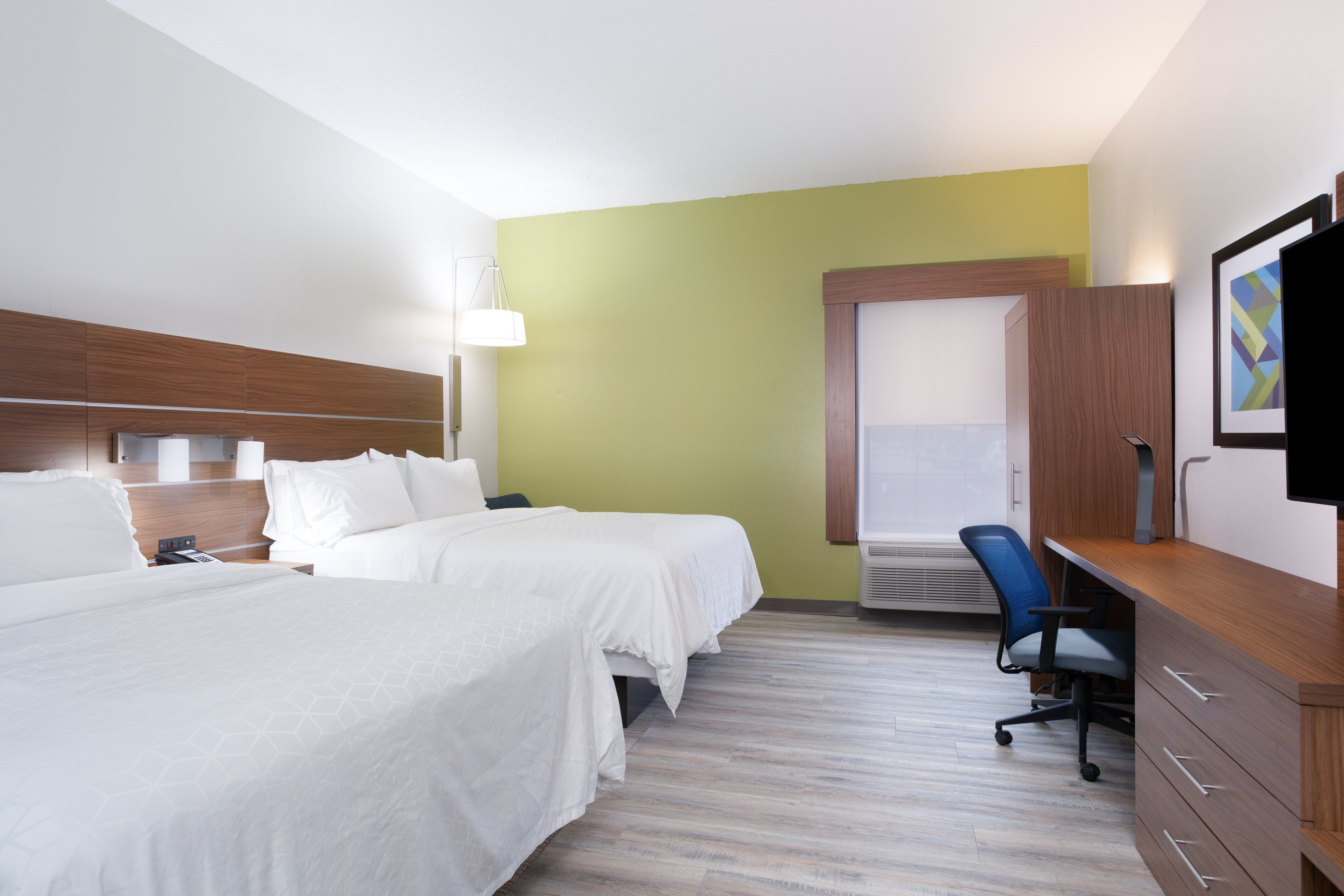 A hotel room with two beds, a desk, a chair, and a television on the wall.