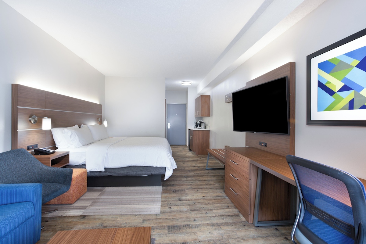 A modern hotel room with a bed, a desk, a TV, and a seating area.