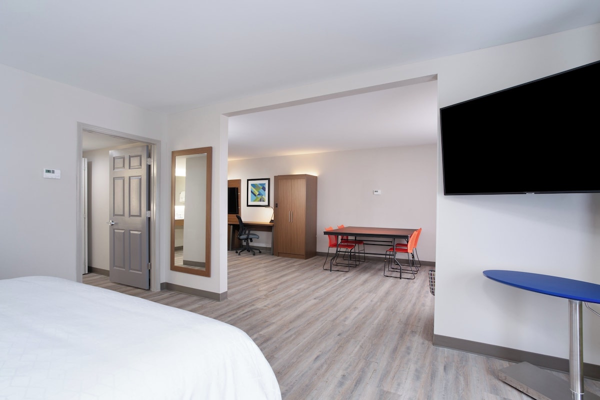A hotel room with a bed, a desk with a chair, a television, and a small table.