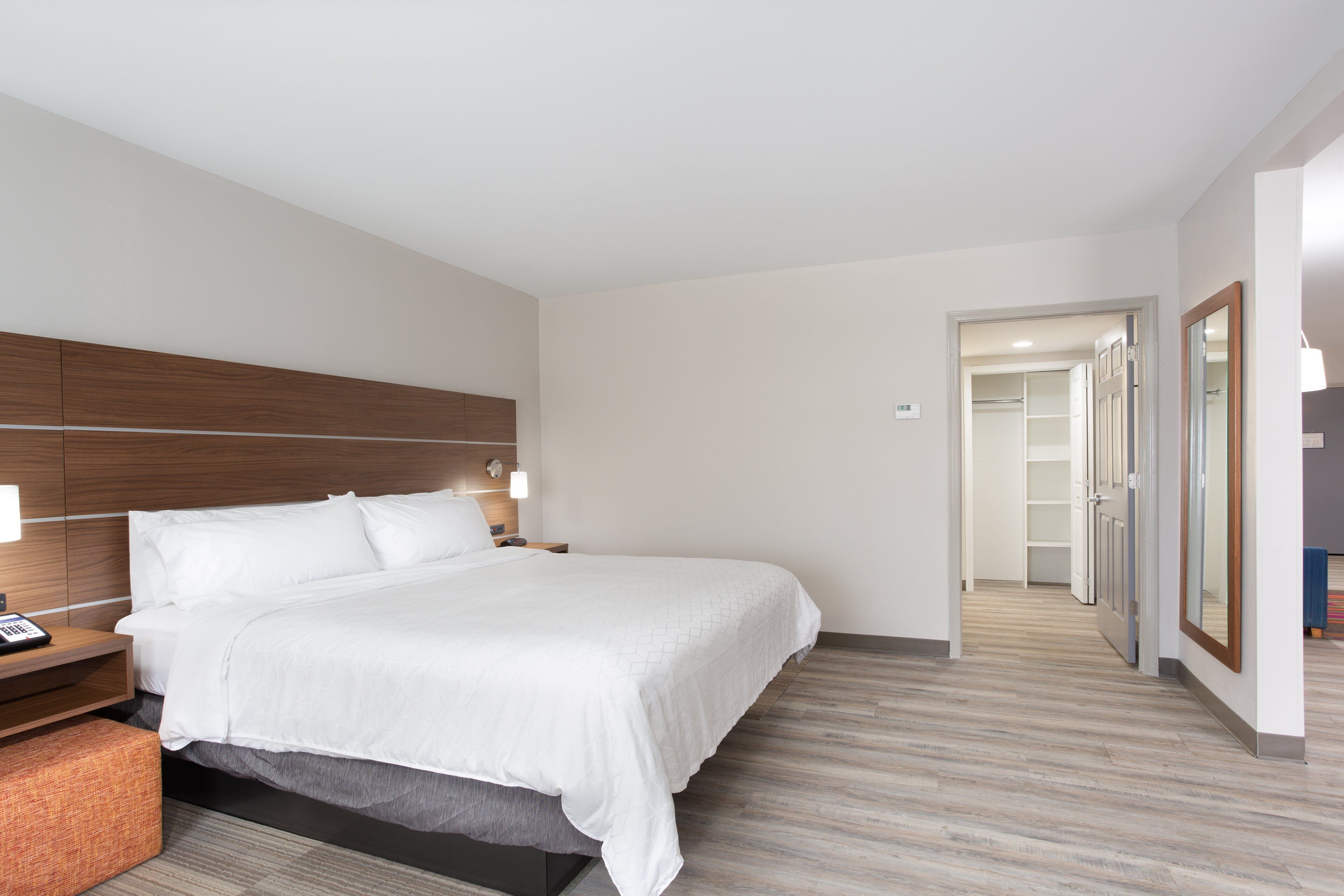 Una habitación de hotel moderna con una cama grande, cabecera de madera, lámparas de noche y un vestidor.