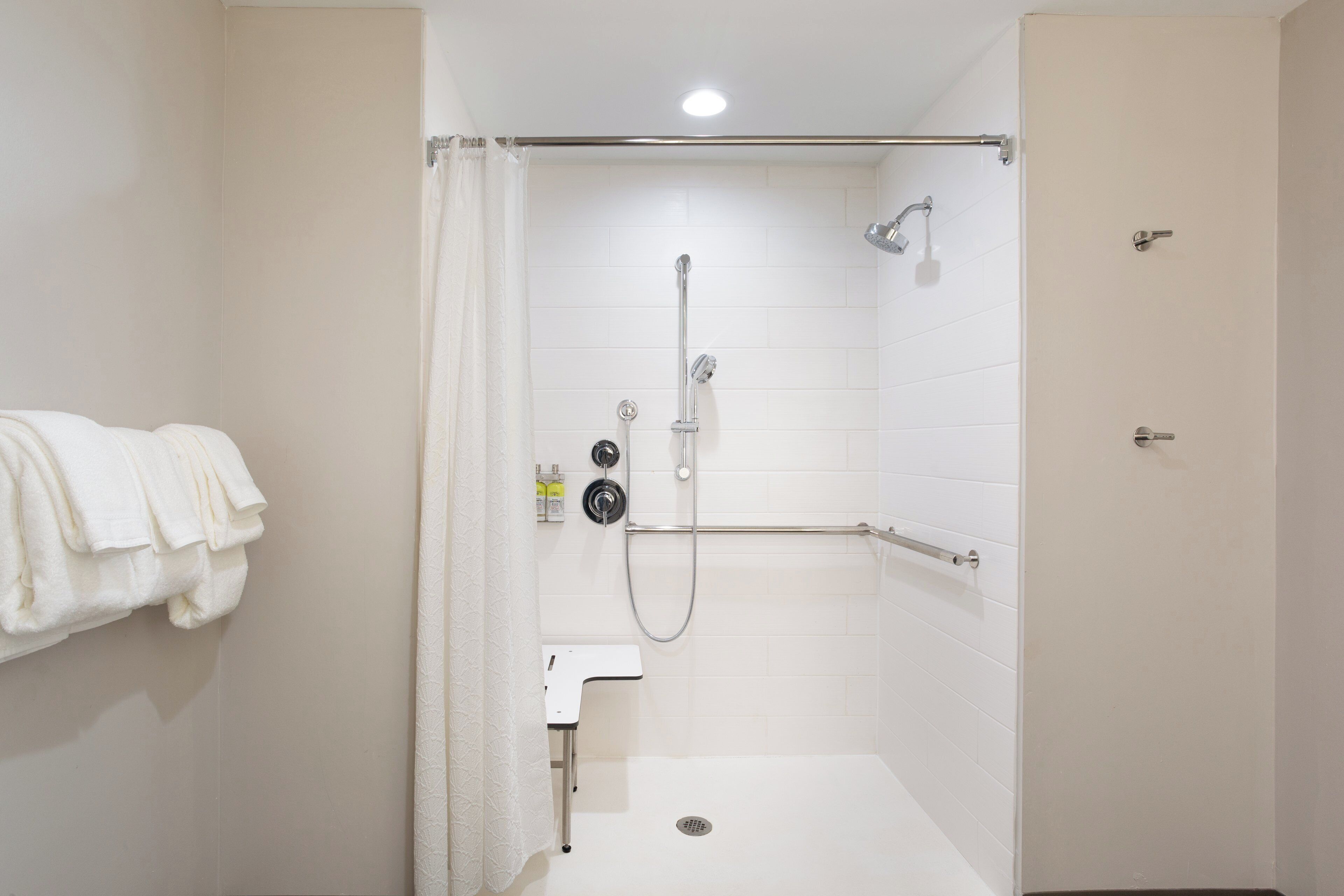 A small, white, walk-in shower with a glass door, a handheld showerhead, a handheld shower attachment, and a wall-mounted faucet.