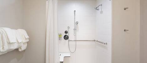 A small, white, walk-in shower with a glass door, a handheld showerhead, a handheld shower attachment, and a wall-mounted faucet.