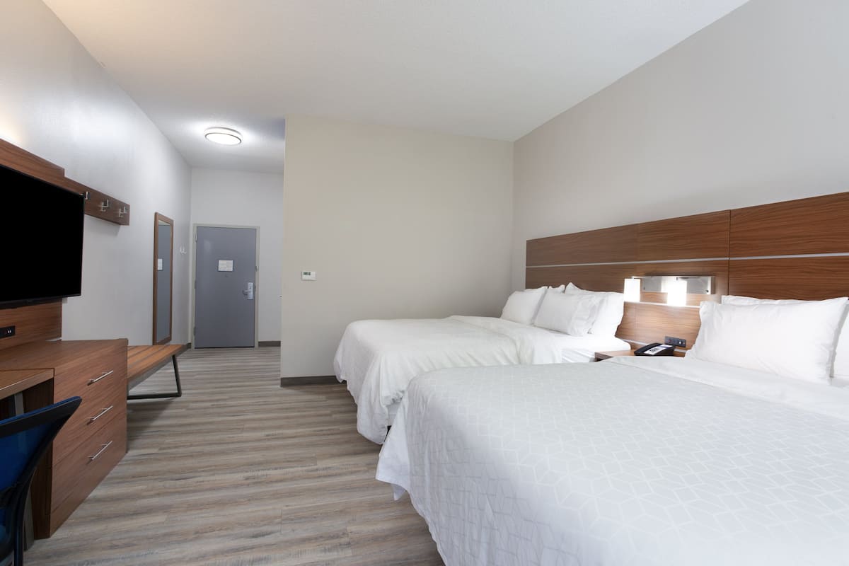 A hotel room with two beds, a desk with a chair, a flat-screen TV, and a door leading to another room.