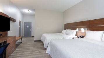 A hotel room with two beds, a desk with a chair, a flat-screen TV, and a door leading to another room.