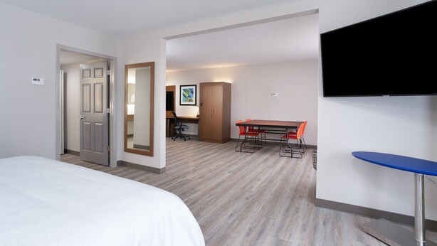 A hotel room with a bed, a desk with a chair, a television, and a dining table with chairs.