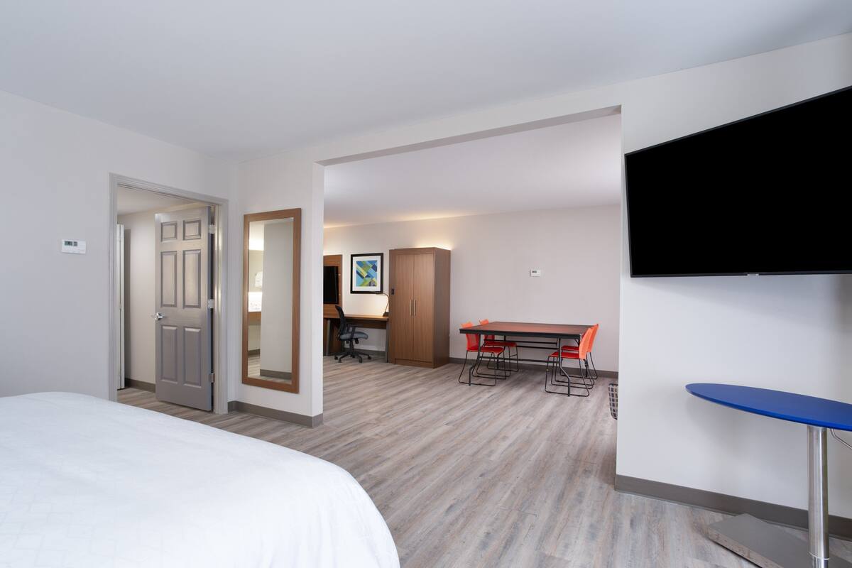 A hotel room with a bed, a desk with a chair, a television, and a dining table with chairs.