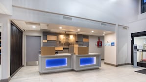 A reception area with a modern design, featuring a counter with illuminated blue panels, a wooden panel wall, and a ceiling with recessed lighting.