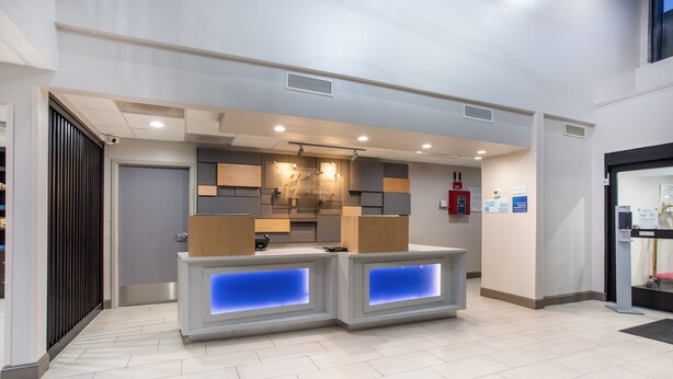 A reception area with a modern design, featuring a counter with illuminated blue panels, a wooden panel wall, and a ceiling with recessed lighting. - Holiday Inn Express Hotel & Suites Morehead Cty by IHG (Morehead City)