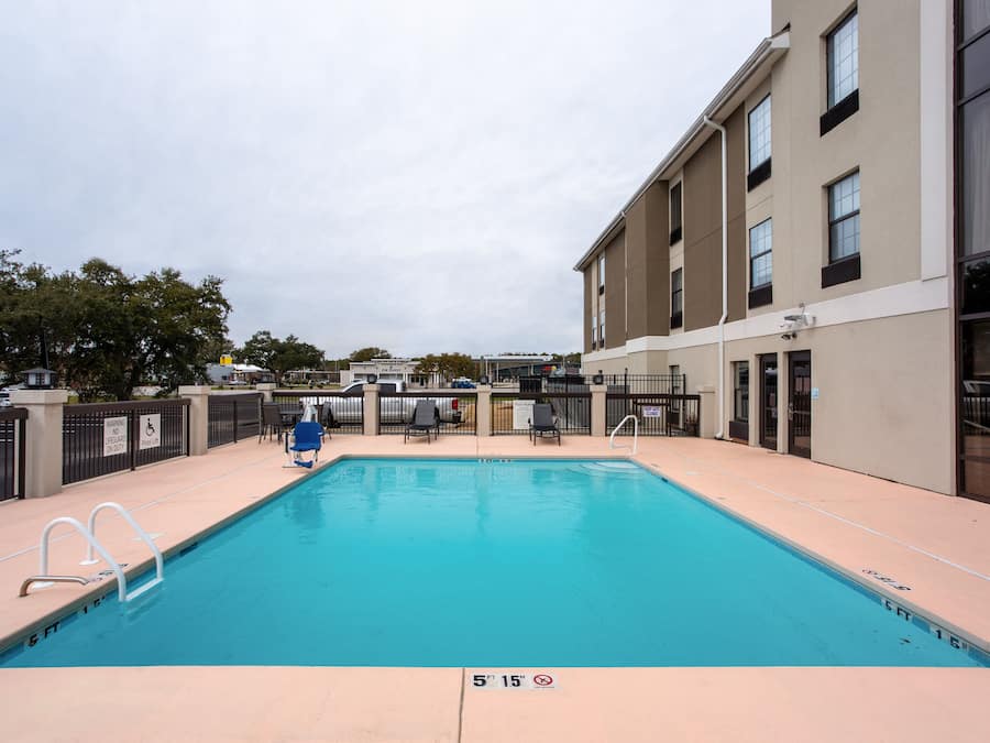 A rectangular pool with a clear blue water surface, surrounded by a beige deck. There are two white pool ladders on the left side.