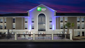 A Holiday Inn Express & Suites building with a prominent entrance, a covered outdoor seating area, and a fenced courtyard.
