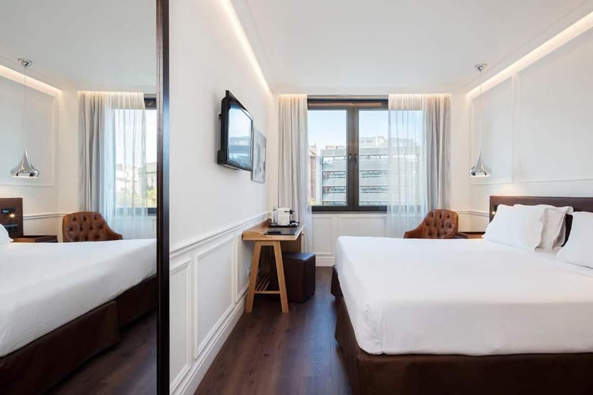 Une chambre d’hôtel avec deux lits, un bureau, une chaise, une télévision et une fenêtre donnant sur un beau paysage.