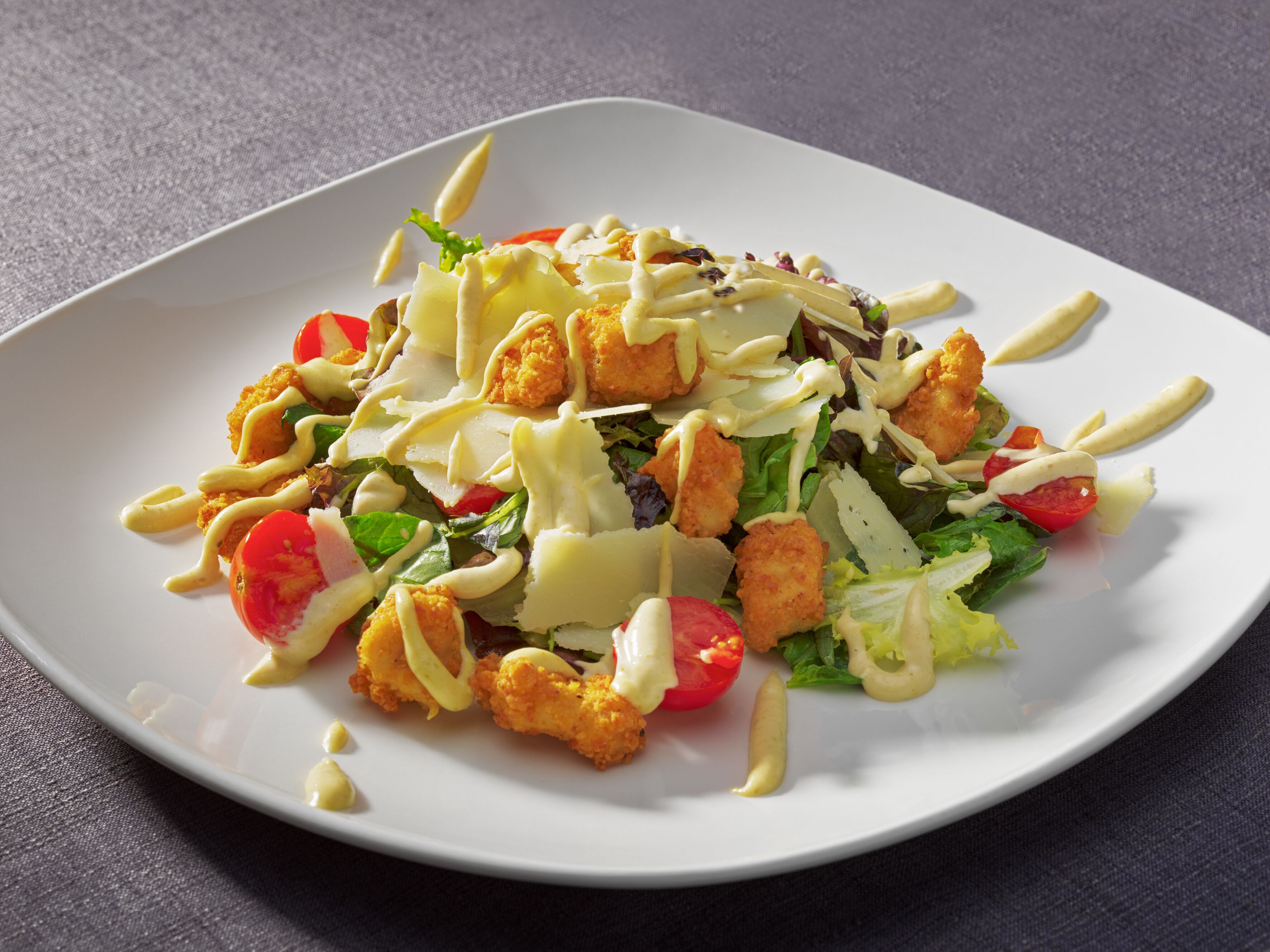 Une assiette blanche contenant une salade composée de laitue, de tomates, de croûtons et d’une sauce crémeuse.