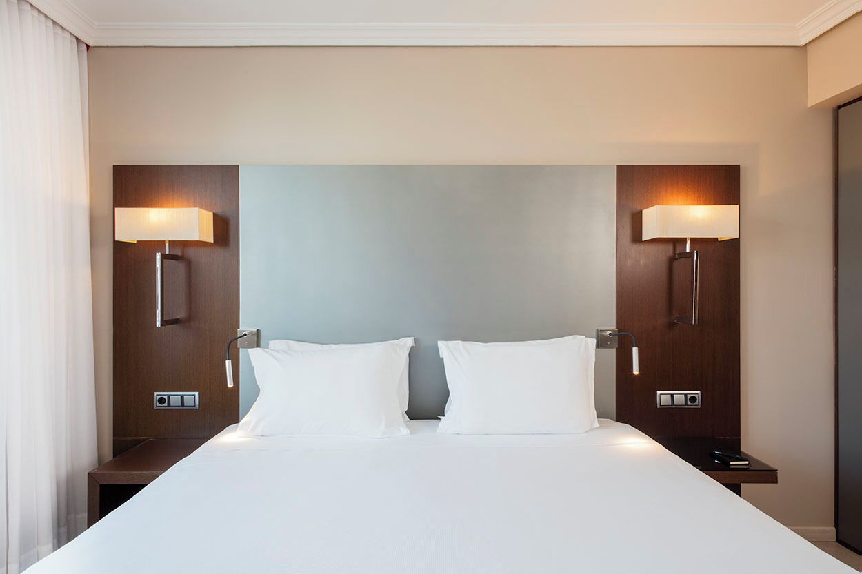 Une chambre d’hôtel avec un grand lit, deux tables de chevet et des lampes fixées au mur.