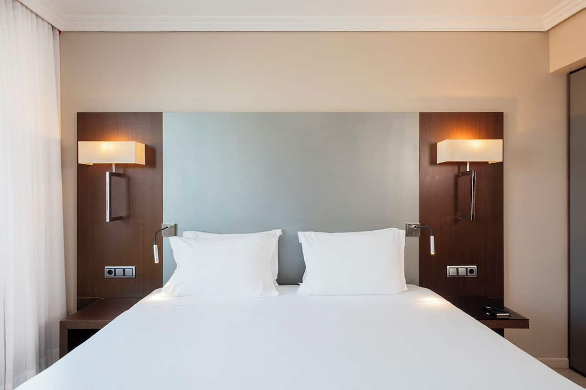 Une chambre d’hôtel avec un grand lit, deux tables de chevet et des lampes fixées au mur.