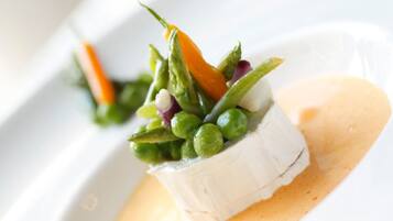 A white plate with a food dish consisting of a white cube, green peas, and a carrot.