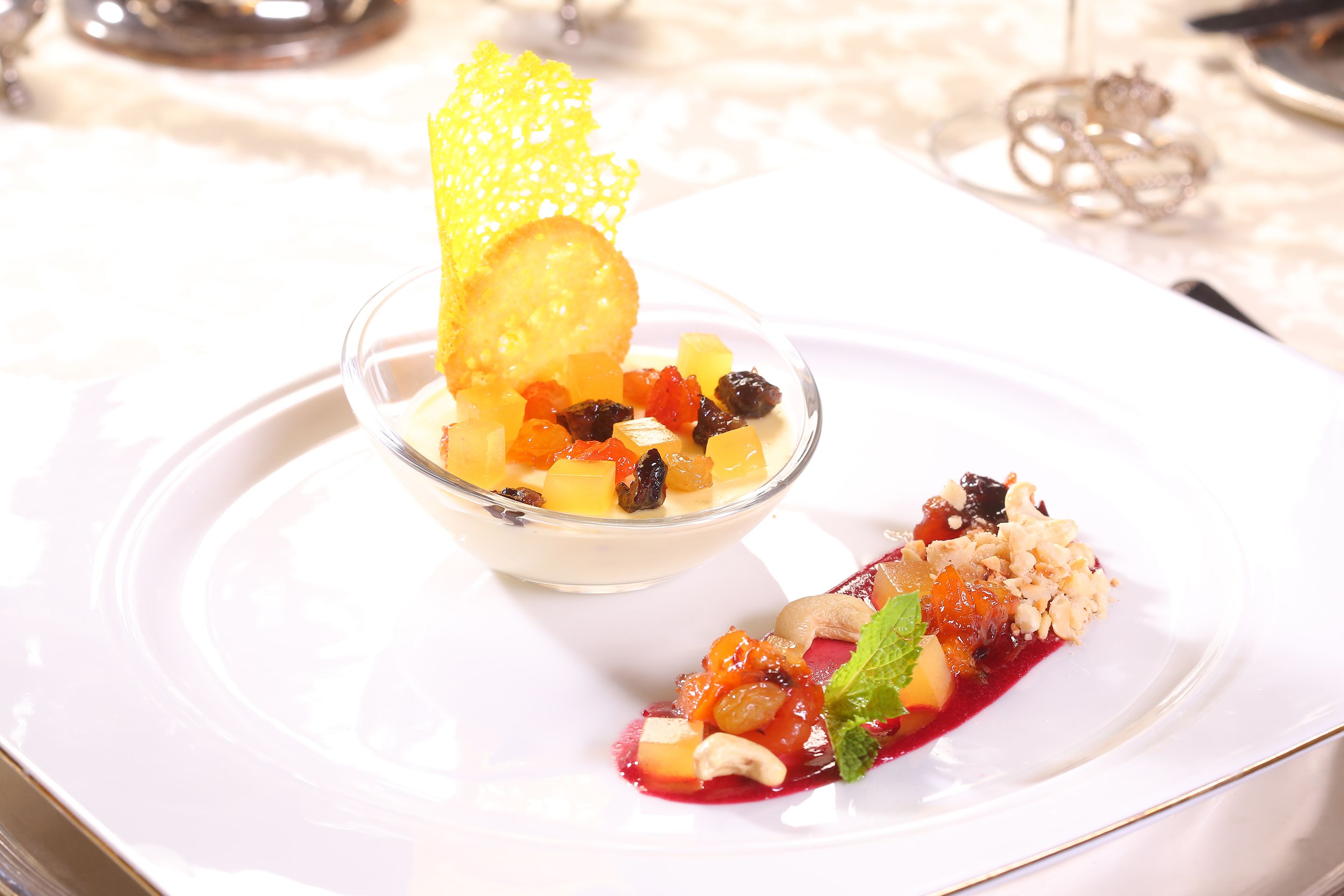 A dessert plate with a variety of fruits and nuts, a decorative yellow element, and a small green leaf garnish.