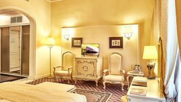 A hotel room with a bed, two armchairs, a vanity with a mirror, a television, and a small table with a lamp.