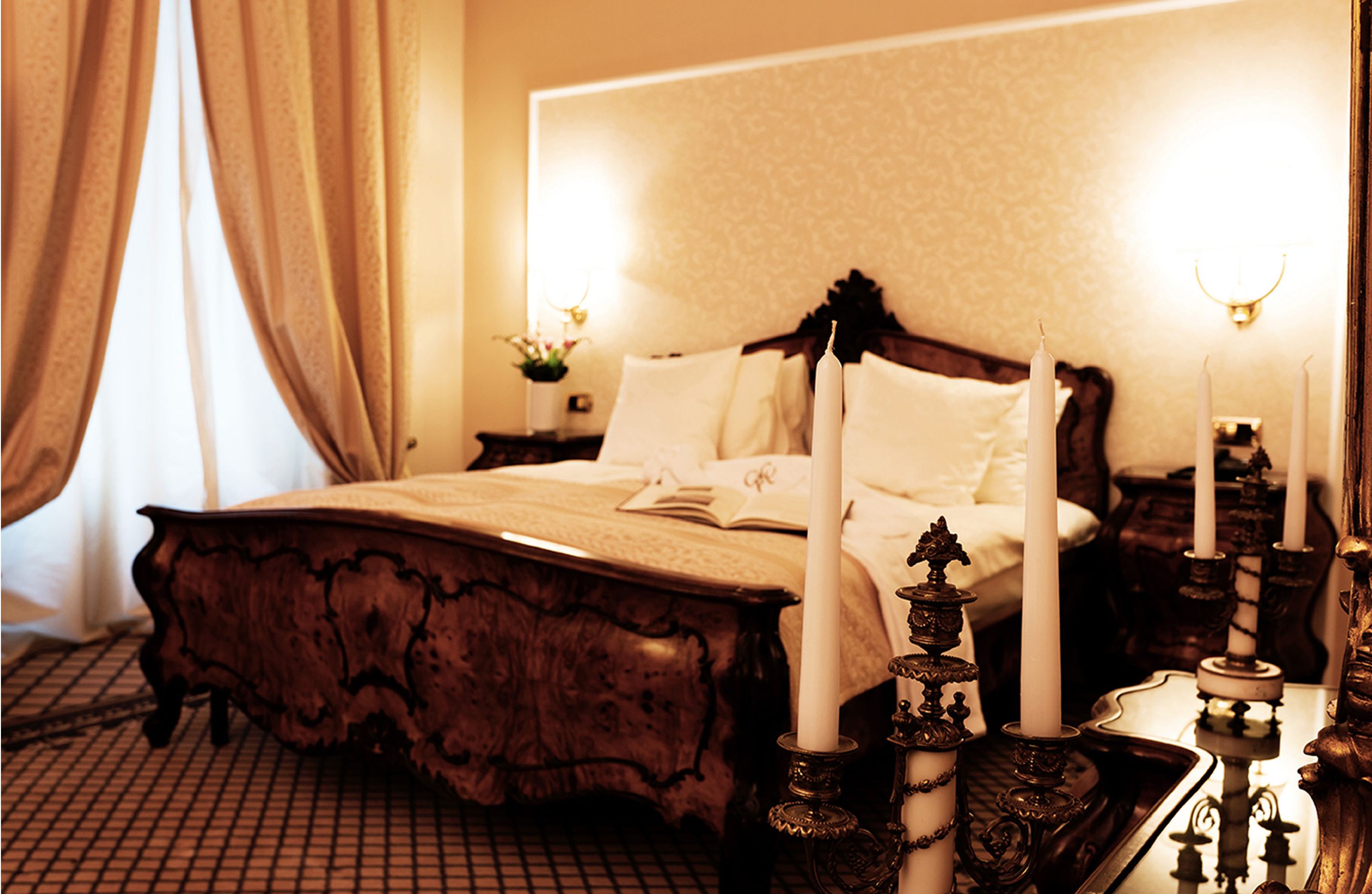 A classic four-poster bed with ornate carvings, a nightstand with a candle holder, and a mirror with a gold frame.