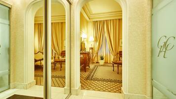 Un vestíbulo de hotel con suelo a cuadros, un mostrador de recepción y una zona de estar con sillas y una mesa.