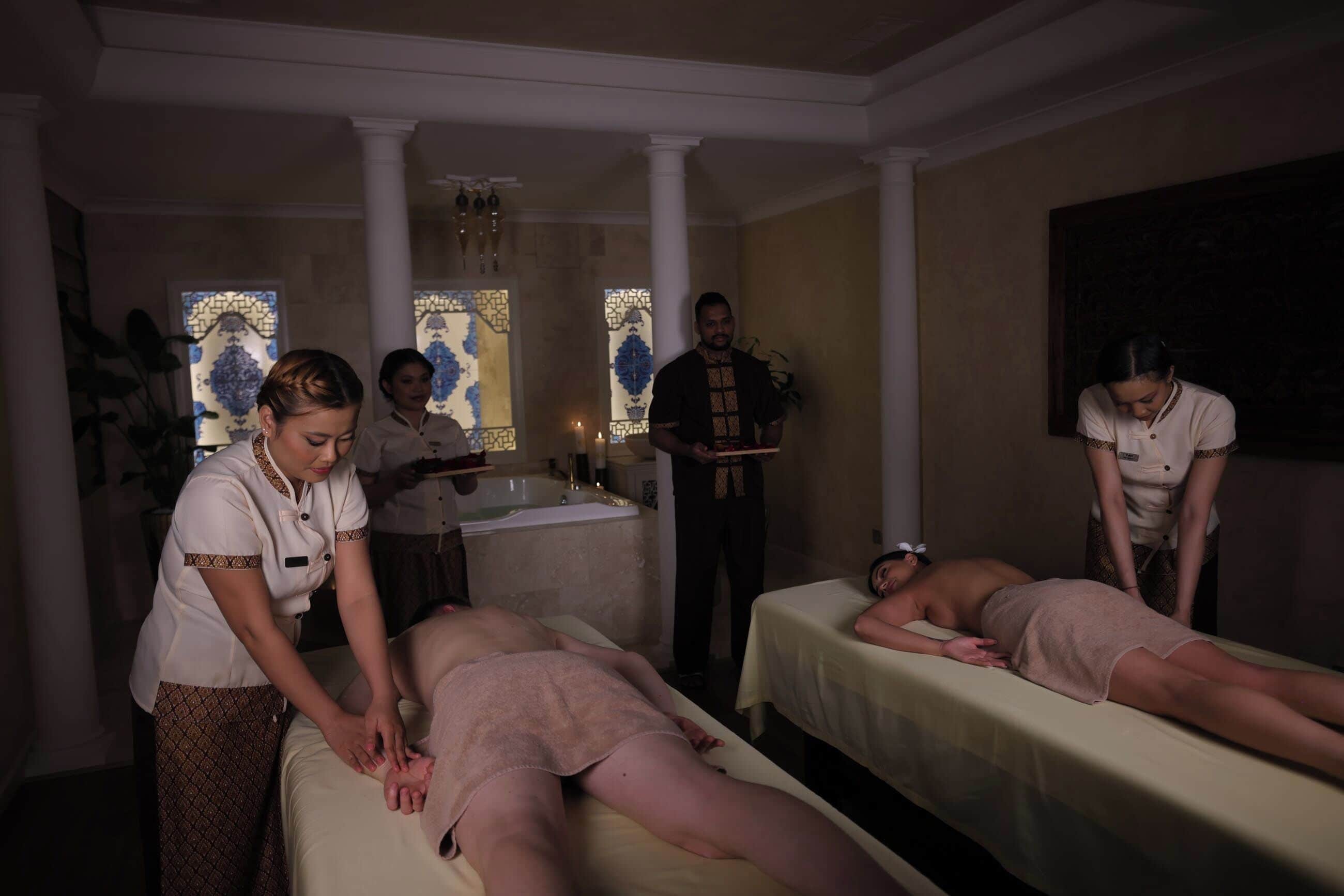 Een spa-ruimte met twee massagetafels, een wastafel en een groot raam met glas-in-lood.