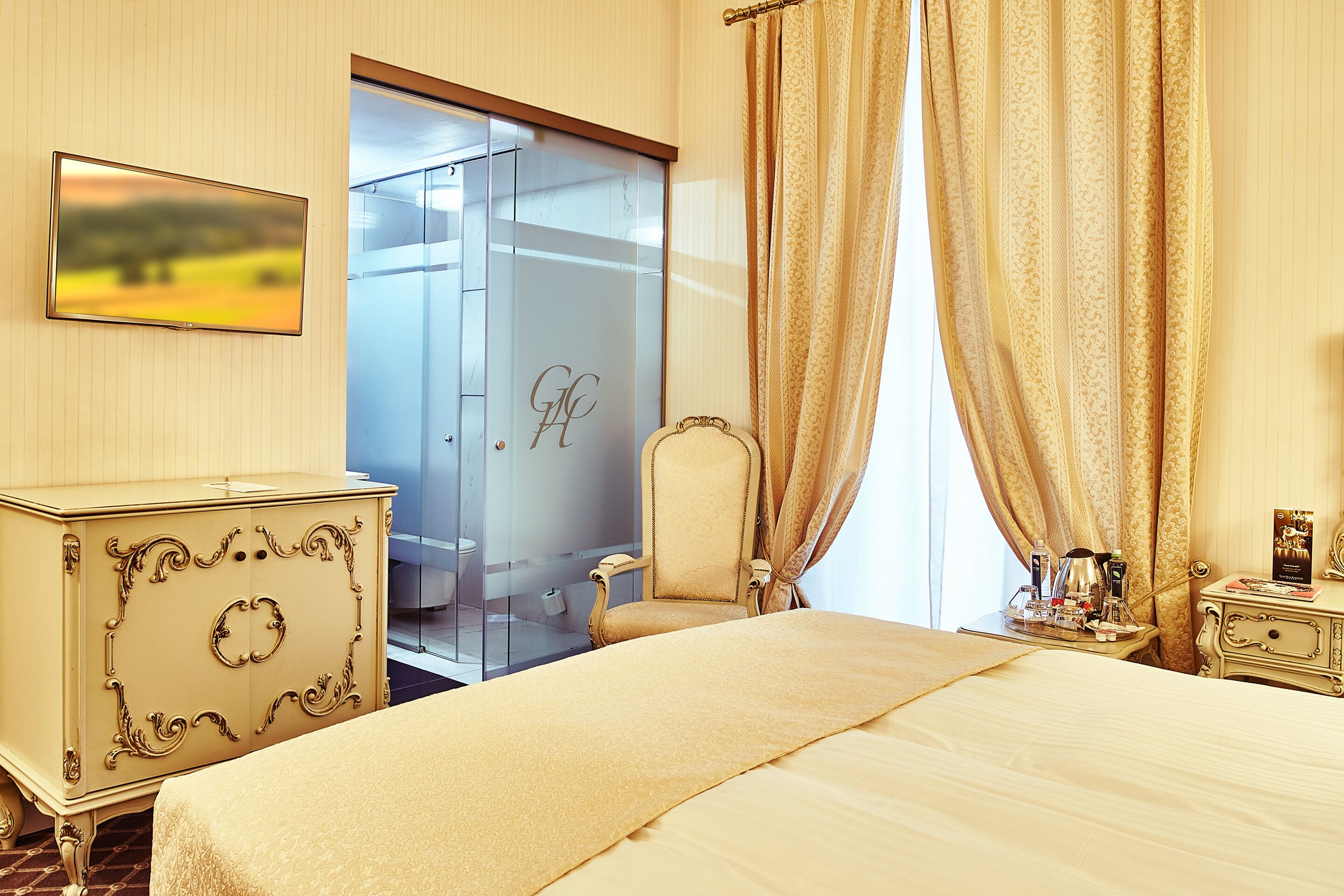 Una habitación de hotel con cama, cómoda, silla, escritorio con lámpara y perchero.