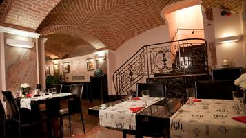 A restaurant with brick ceiling, black metal staircase, and tables set with white tablecloths.