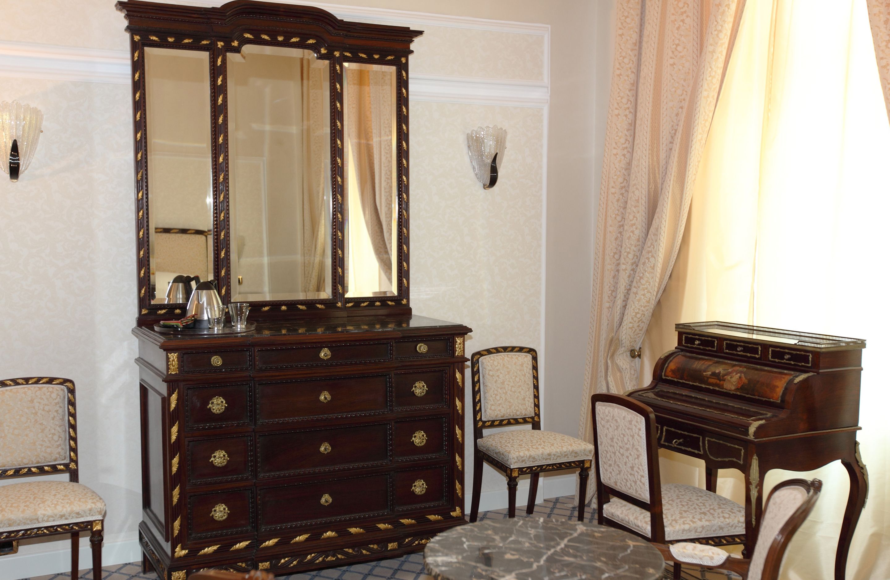 A room with a large wooden dresser, two chairs, a small table, and a piano.