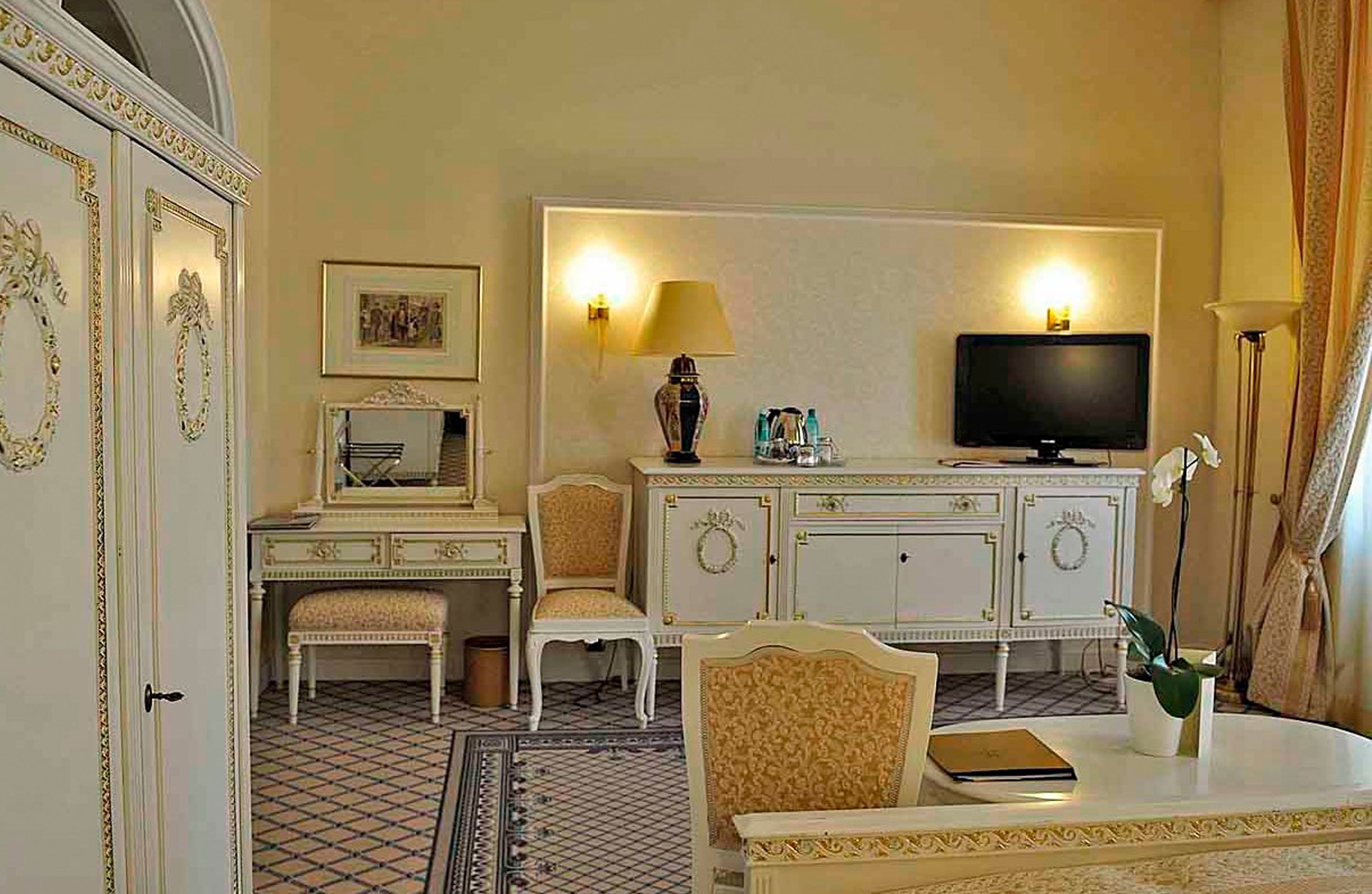A hotel room with a bed, a desk with a chair, a television, and a small table with a plant.