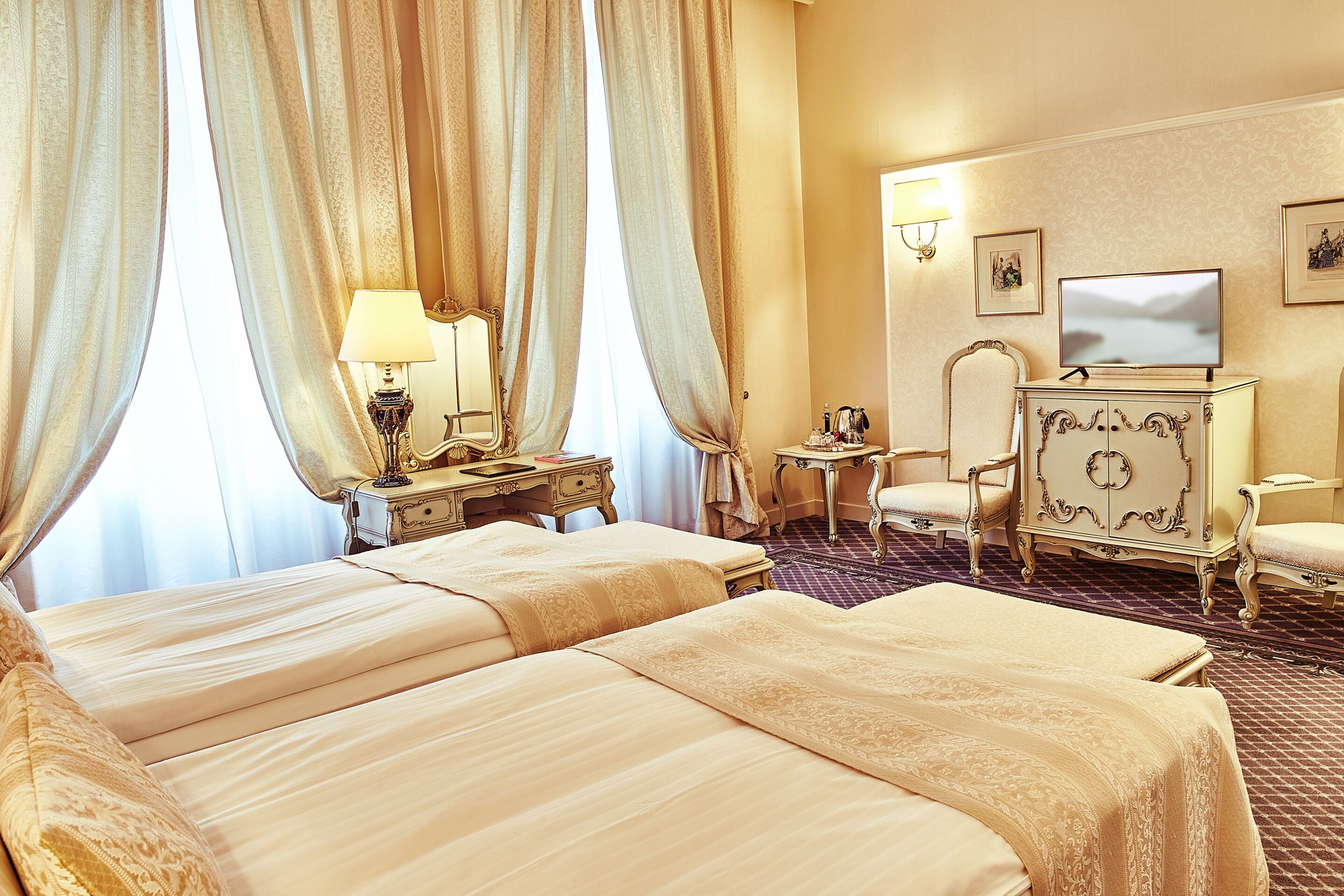 Habitación de hotel con dos camas, un escritorio con lámpara, televisor y cómoda.