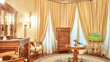 A room with a wooden desk, a chair, a television on a stand, a cabinet, and a patterned rug.