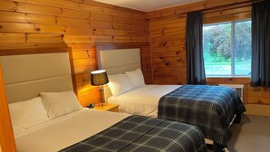 A room with two beds, wooden walls, a nightstand with a lamp, and a window with curtains. - Northern Lights Lodge (Stowe)
