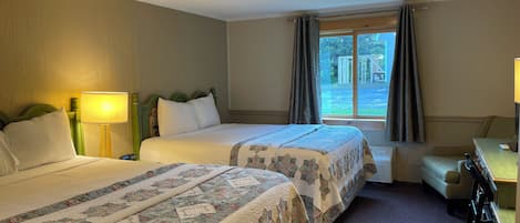 A hotel room with two beds, a desk, a chair, and a window with curtains.