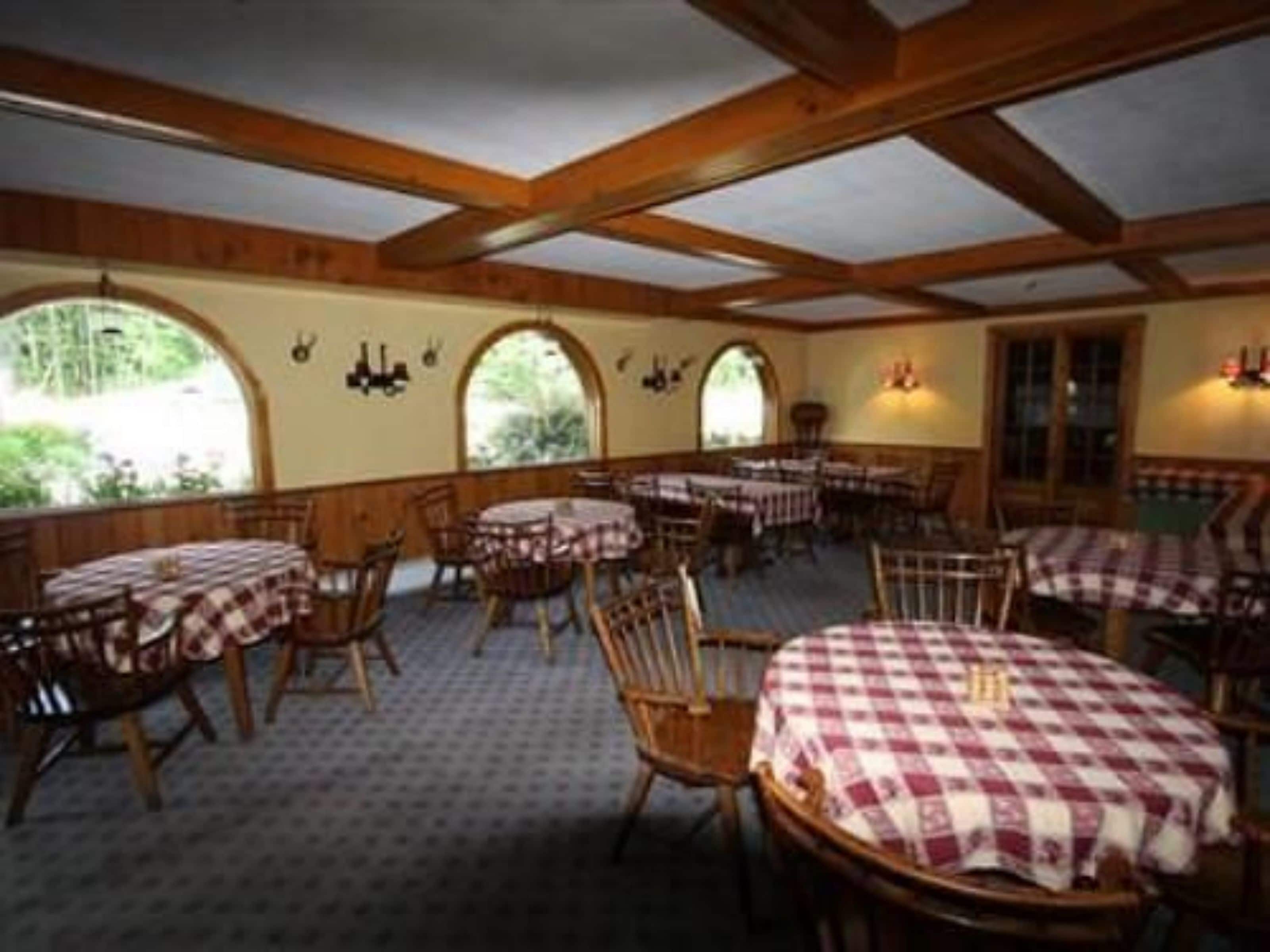 Un comedor con mesas y sillas de madera, cubiertas con manteles a cuadros, y ventanas amplias con arcos.