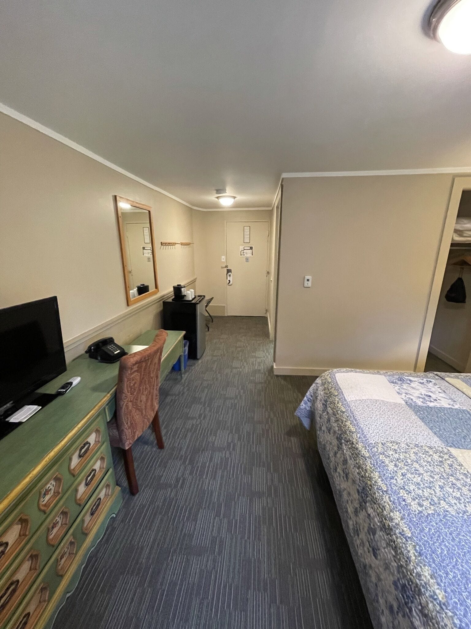 A hotel room with a bed, a desk with a computer, a television, a dresser, and a mirror.