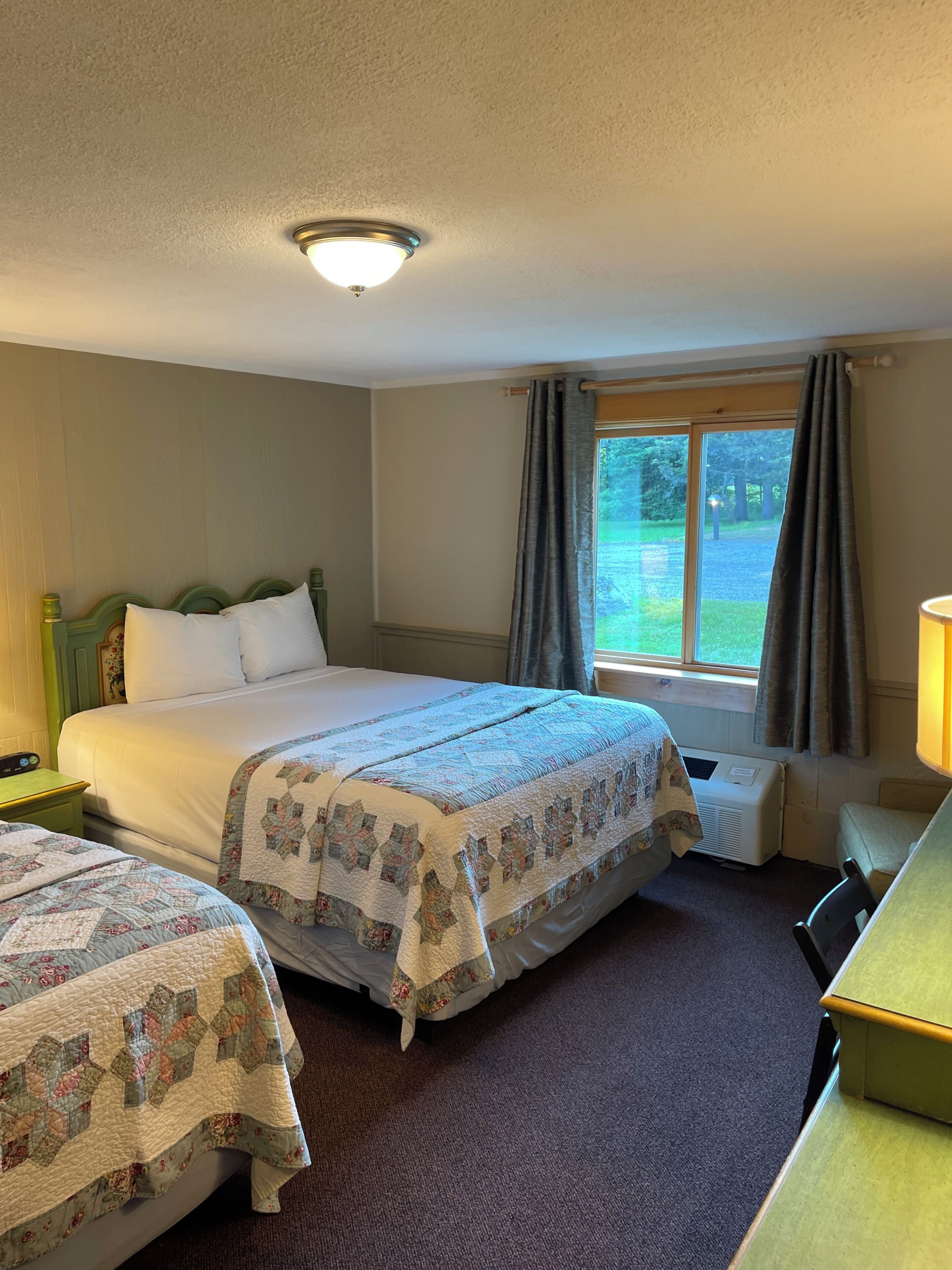Une chambre d’hôtel avec deux lits, un bureau, une chaise, une fenêtre avec des rideaux et un luminaire au plafond.