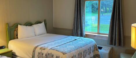 Une chambre d’hôtel avec deux lits, un bureau, une chaise, une fenêtre avec des rideaux et un luminaire au plafond.