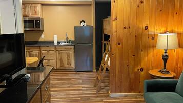 A compact kitchen with wooden cabinets, a microwave, a refrigerator, and a dining area with a table and chairs.