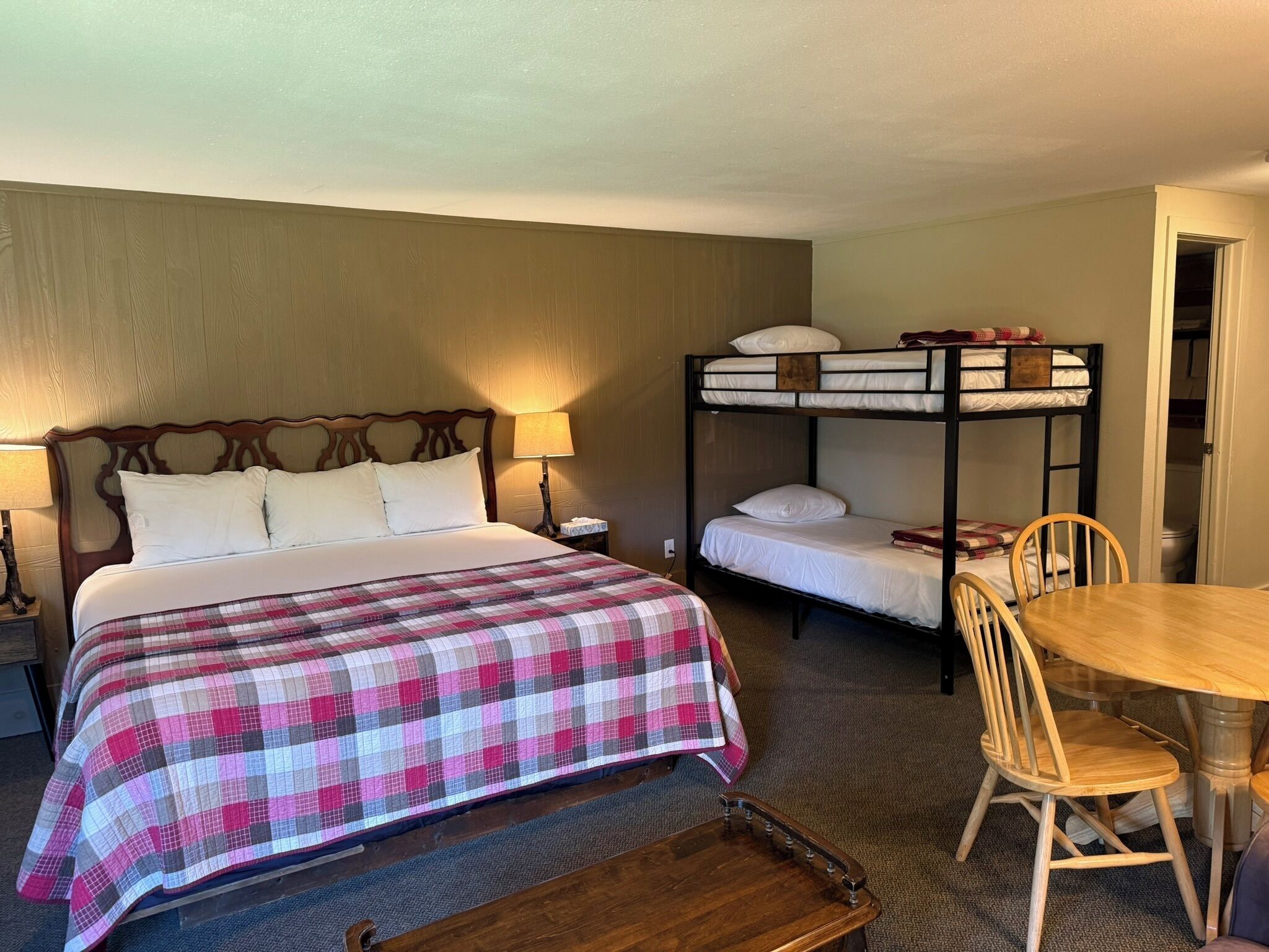 Une chambre d’hôtel avec un lit simple, un lit superposé, une table en bois et une chaise.