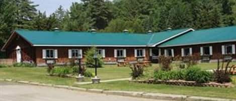 A two-story lodge with a green roof, surrounded by dense forest.