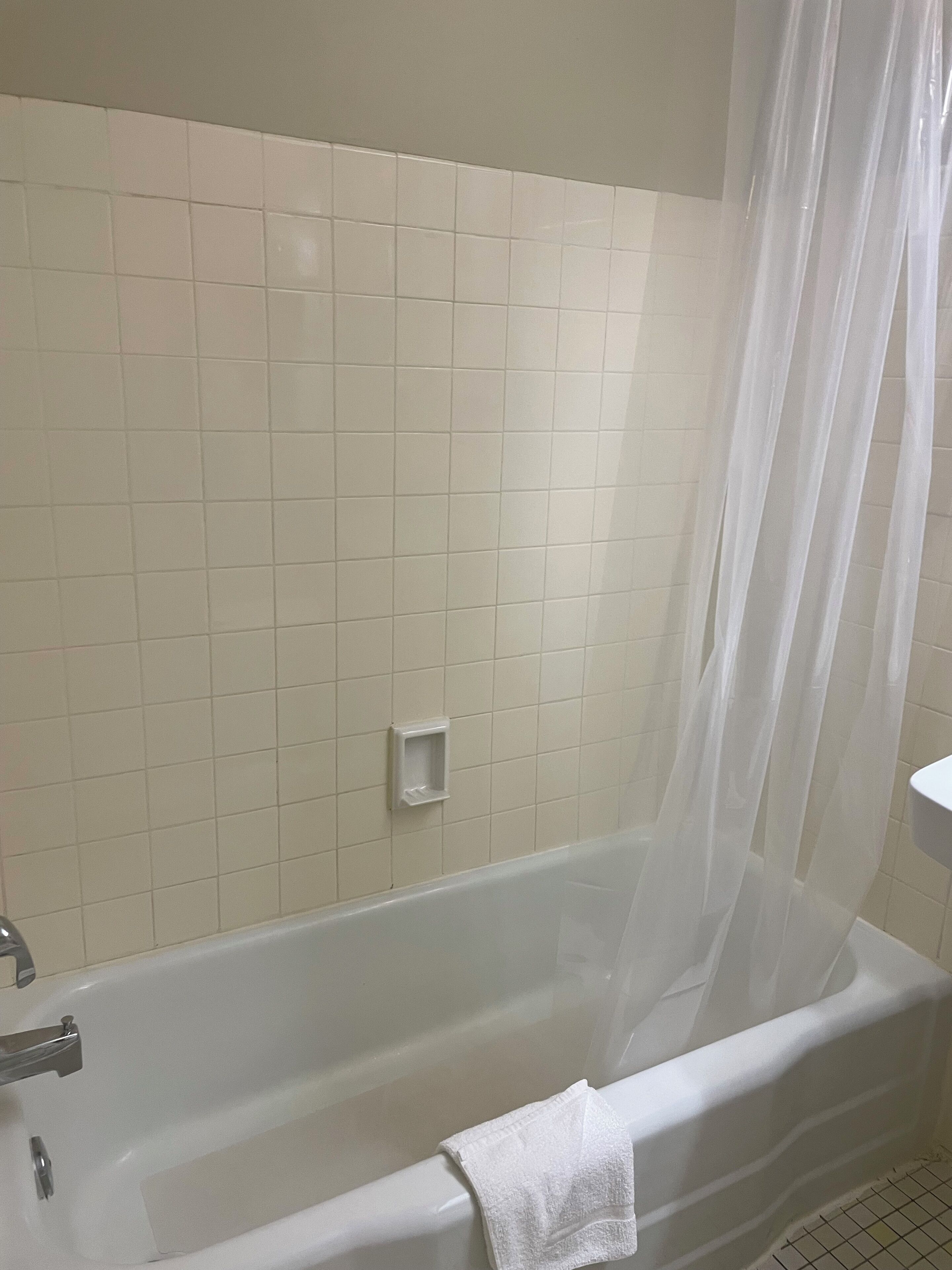 A bathroom with a bathtub, a white tiled wall, and a shower curtain.