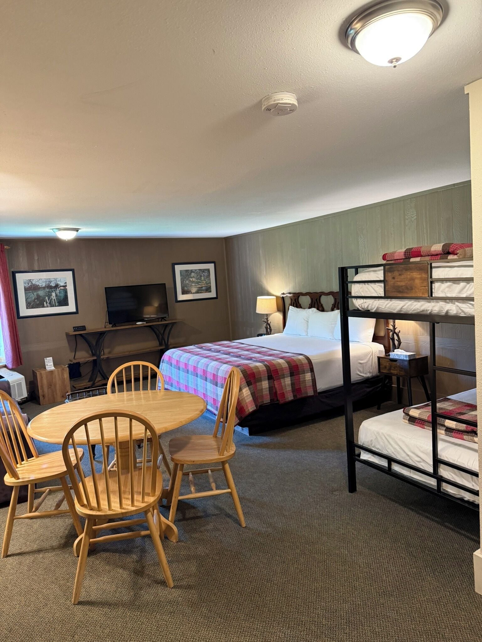 A hotel room with bunk beds, a round wooden table with chairs, a television, and framed pictures on the wall.