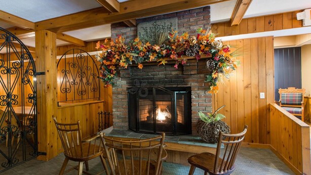 A cozy room with a fireplace, wooden walls, and a dining area with chairs. - Northern Lights Lodge (Stowe)