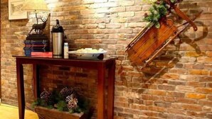 A rustic brick wall with a wooden coat rack holding a plant and a decorative item. A table with books, a lamp, and a thermos is in front of the wall. - Northern Lights Lodge (Stowe)