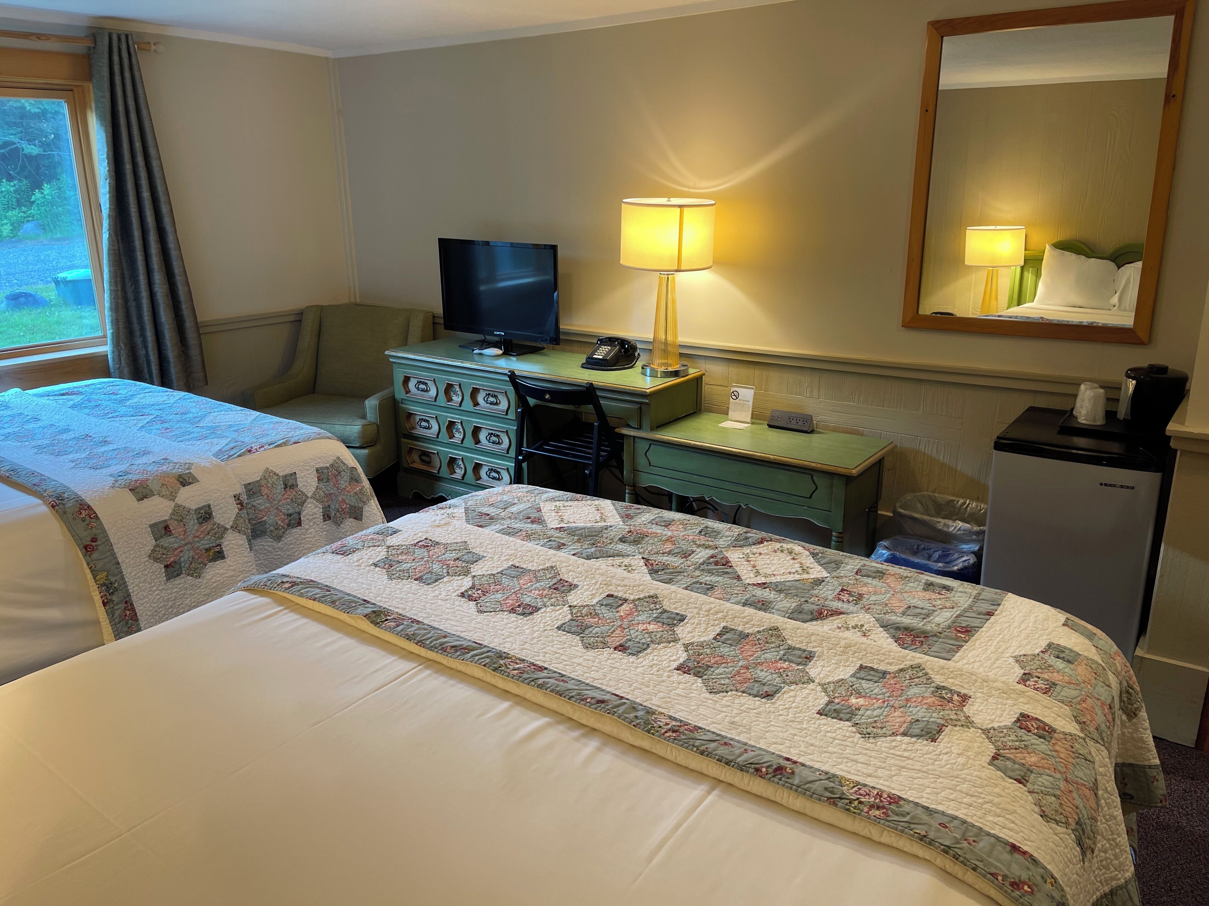 A hotel room with a bed, a desk, a television, a lamp, and a refrigerator.